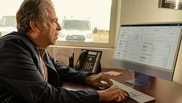 Woman checks vehicle data on a tablet near a parked pickup truck, showcasing remote monitoring technology.