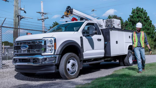 Utility work truck with a crane parked near power lines; worker in safety gear walking nearby.