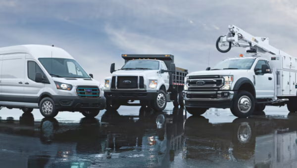 Three Ford commercial trucks, including a transit van, dump truck, and utility truck, on a reflective surface.