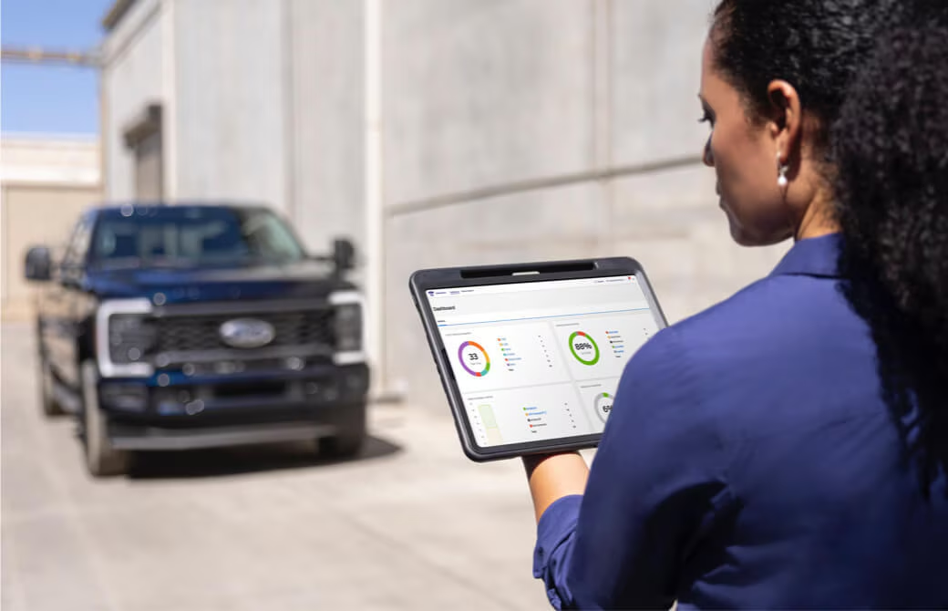 Woman checks vehicle data on a tablet near a parked pickup truck, showcasing remote monitoring technology.