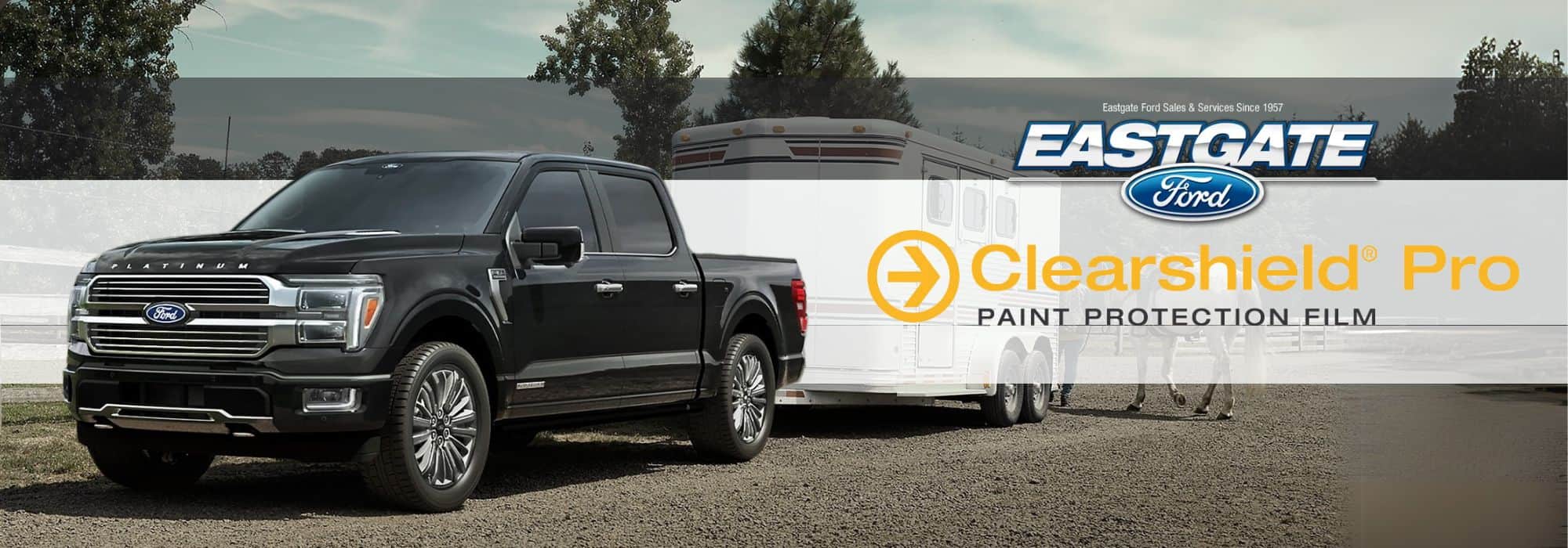 Black Ford truck towing a trailer, featuring Eastgate Ford and Clearshield Pro paint protection film logos.