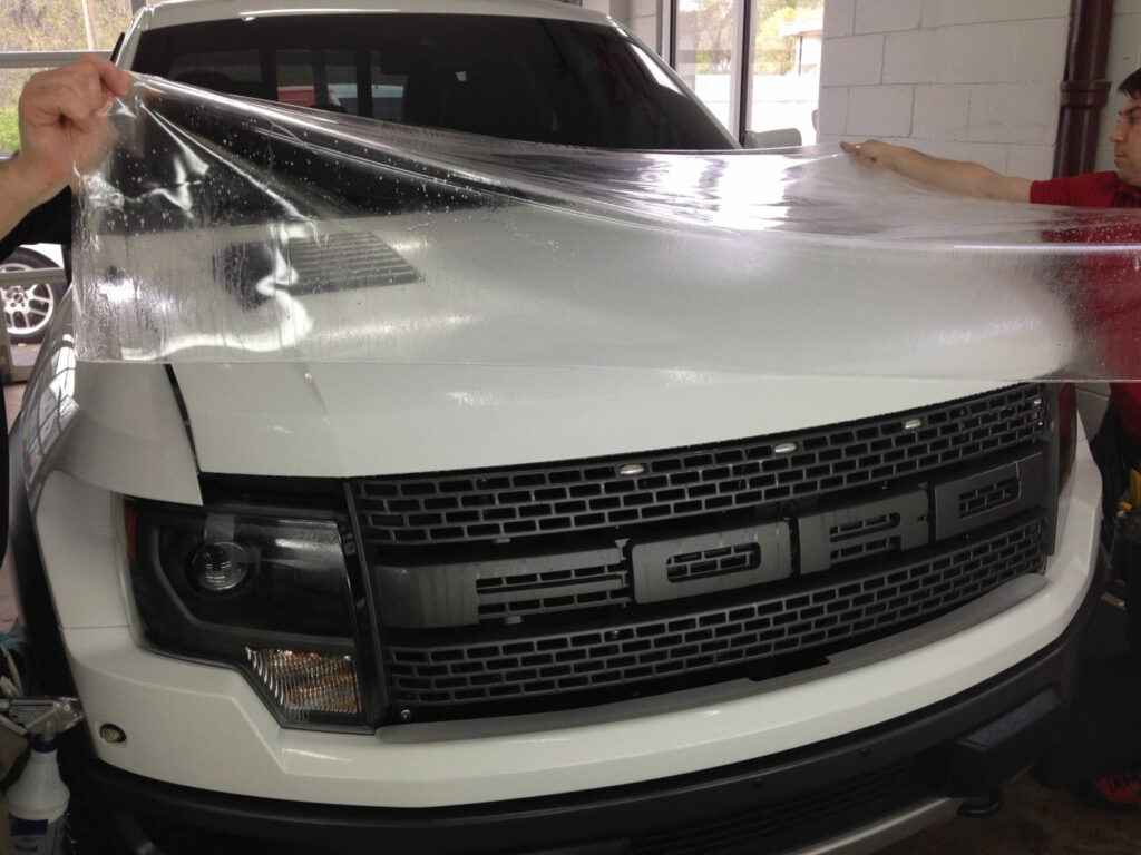 Applying clear protective film on a white truck's front for paint protection. Auto detailing service.